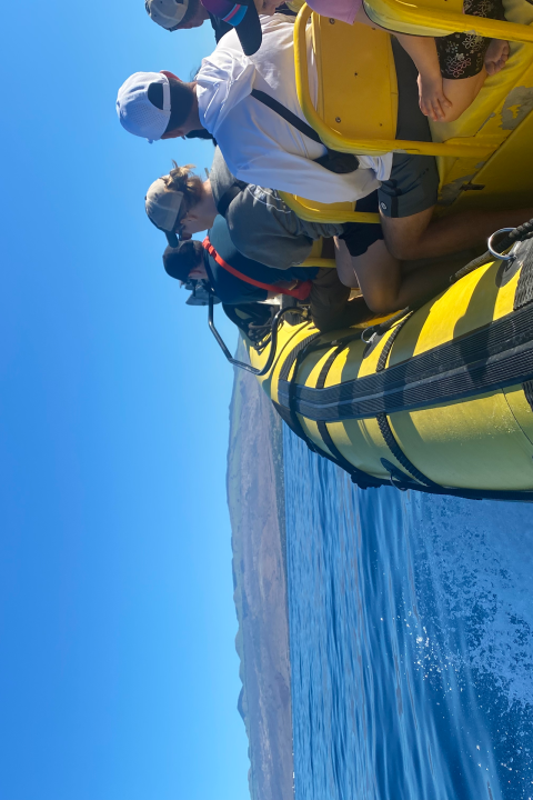 People riding on a yellow inflatable boat on clear blue water.
